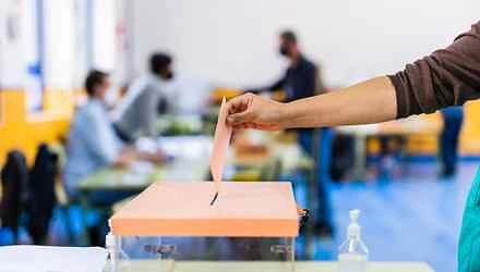 Person an einer Wahlurne mit einem Wahlzettel in der Hand